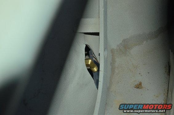 Brass fitting and black hose visible through a hole in a gray metal panel