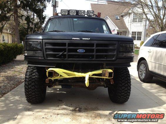 Black Ford F-Series truck with aftermarket lights on the roof and a yellow strap on the front bumper