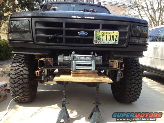 Front of a black Ford truck on jack stands, showing a winch mounted below the grille. New Jersey license plate P13AZ