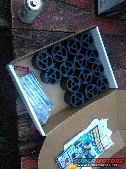 Box of lift kit pucks and hardware, with a can of beer and some papers on a wooden surface