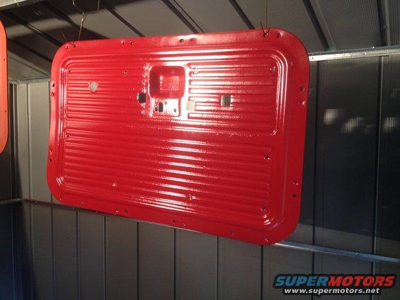 Red painted truck door panel hanging, showing horizontal ridges and mounting holes