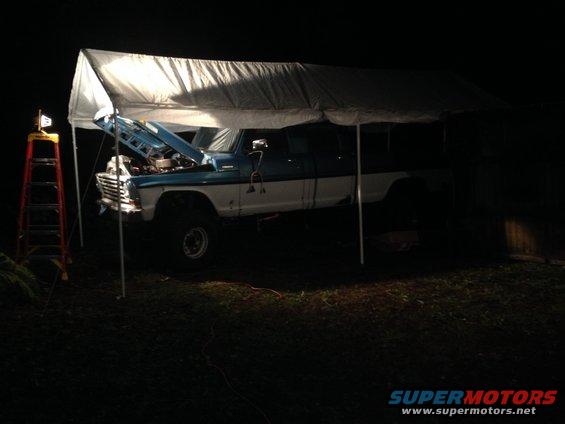 Blue and white Ford pickup truck with hood open under a canopy at night