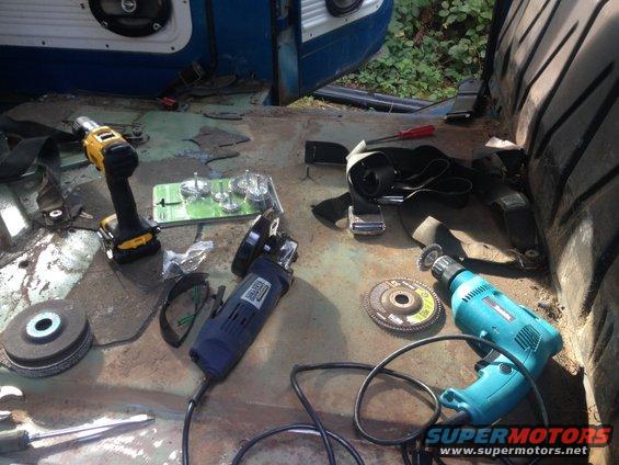 Tools like a drill and grinder are laid out on the floor of a vehicle interior, possibly for restoration