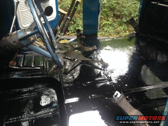 Interior floor of a truck with black coating and steering column visible