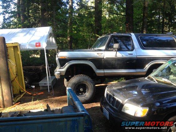 Black and silver Ford Bronco with lifted suspension and large tires, parked outdoors next to a black SUV