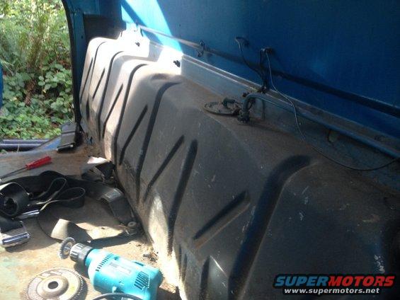 Close-up of a large plastic fuel tank inside a vehicle, with a drill and screwdriver nearby