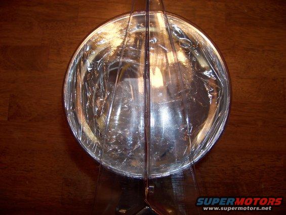 Headlight reflector with clear plastic protective wrap, on a wooden surface