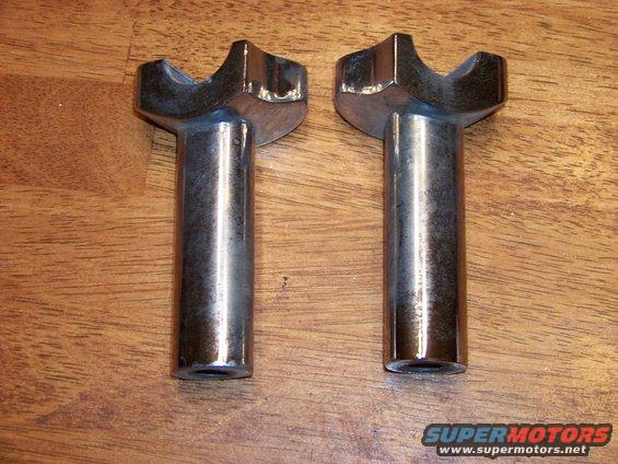 Two chrome-plated metal automotive parts with a Y-shaped top, resting on a wooden surface