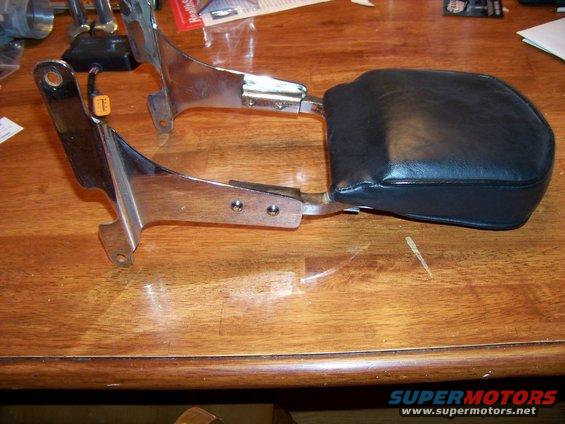 Black leather motorcycle backrest with chrome mounting brackets on a wooden table
