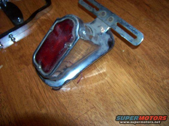 Chrome tail light assembly with red lens and adjustable metal bracket on wooden surface