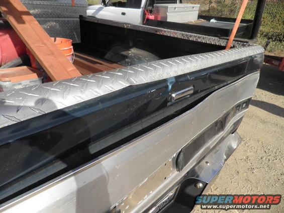 Rear view of a truck bed with diamond plate trim and tools; another truck is visible behind it