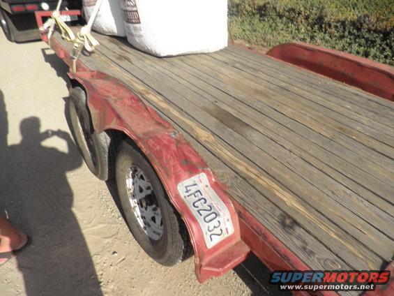 Red trailer bed with wooden planks, carrying two large white bags of seed. License plate reads 4FC2032
