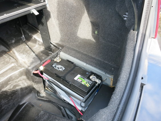 Car battery with red and black cables in a vehicle's trunk compartment