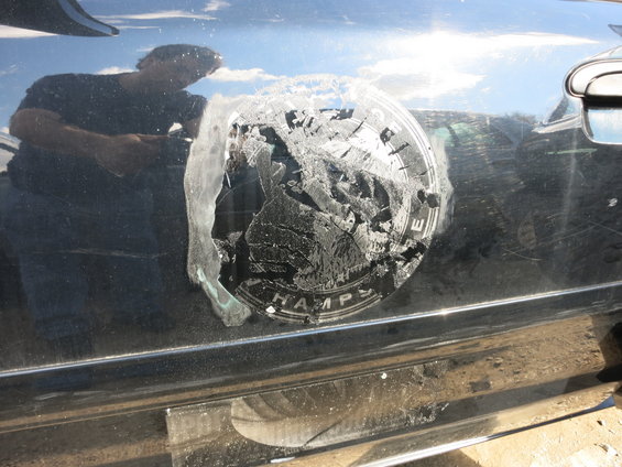 Black car door with a circular emblem that reads "CHAMPS" and shows a landscape, partially peeled off