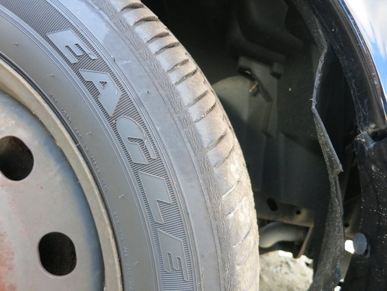 Close-up of a car's front tire and wheel well. The tire has some text on it