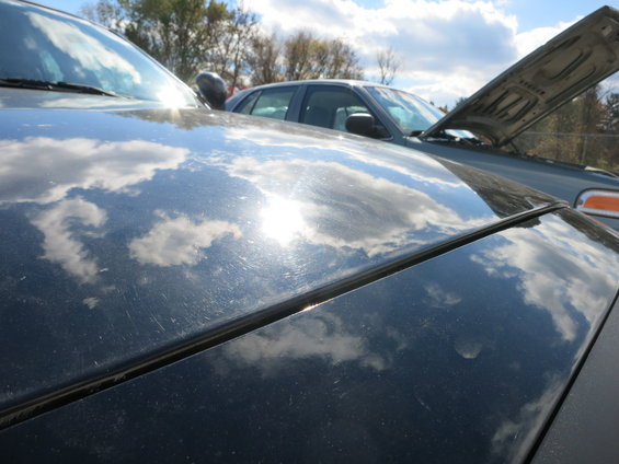 Reflection of clouds on a car hood, with another car parked behind it, hood up