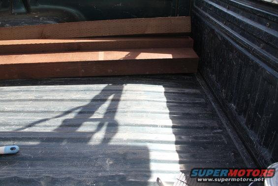 Truck bed loaded with lumber, showing the ribbed floor and side panel. Shadow of a person is visible