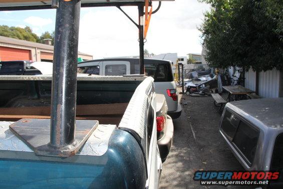 Close-up of a pickup truck bed rack, with other vehicles and a junkyard scene in the background