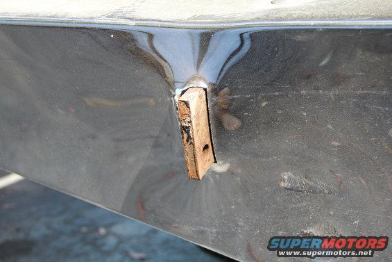 Close-up of a dark-colored vehicle body panel with a wooden block inserted into a hole