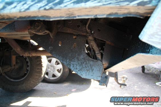 Undercarriage view showing a hitch receiver and suspension components. Another vehicle's wheel is visible in the background