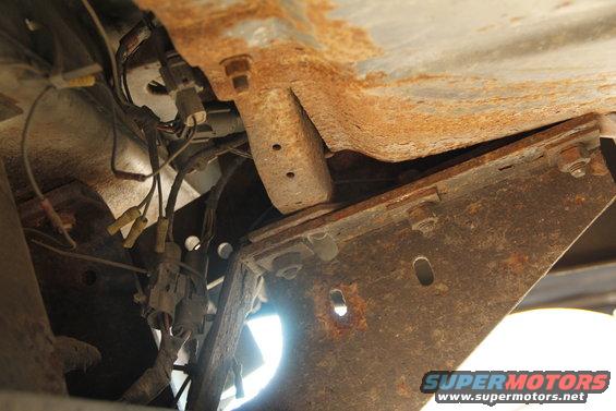Underside of a rusty vehicle frame showing wiring and mounting brackets