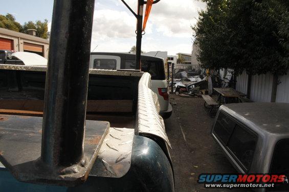 Close-up of a truck bed with a white SUV and a camper shell in the background