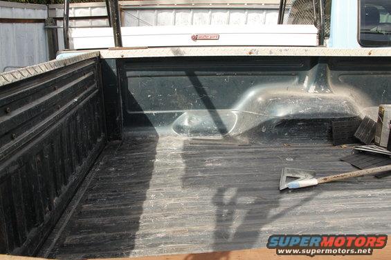 Truck bed with a toolbox and ladder rack, showing wear and tear. A shovel rests inside
