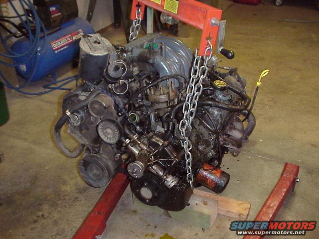 Engine on a red engine stand, suspended by chains from an engine hoist. An air compressor is in the background