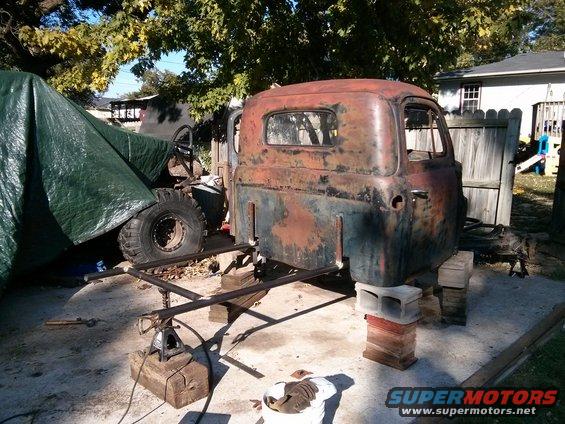 rusted truck cab on cinder blocks with tarp-covered object to the left