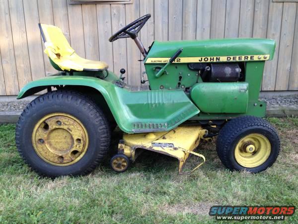 Green John Deere lawn tractor with yellow seat parked on grass next to a wooden building