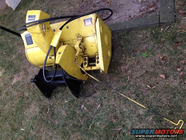 Yellow snow blower attachment with black chute and yellow handle. Caution labels visible