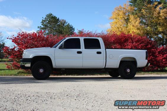 White 2006 Chevrolet Silverado 2500 pickup truck parked on a gravel road with red and yellow trees behind it