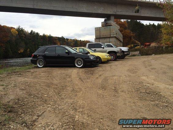 Black station wagon, yellow sedan, and two pickup trucks parked under a bridge