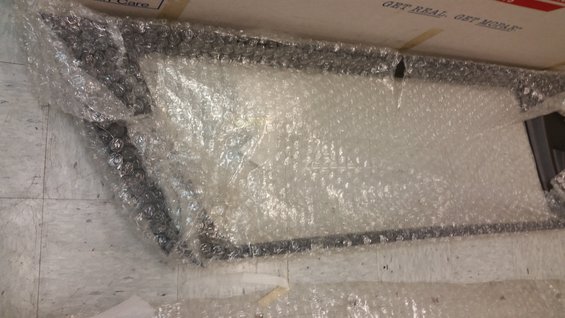 Partially unwrapped rectangular object with dark frame and white interior, covered in bubble wrap