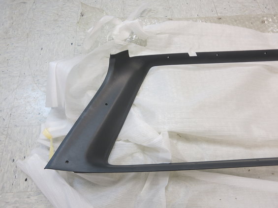 Dark gray plastic trim piece, possibly for a vehicle window frame, lying on white protective material