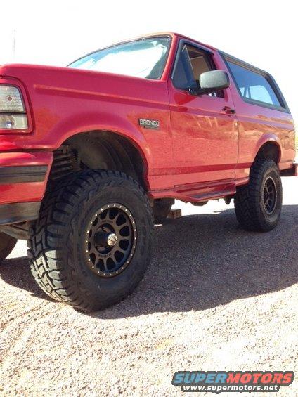 Red Ford Bronco with aftermarket wheels and tires, parked on gravel