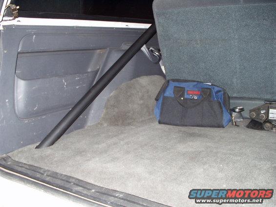 Interior cargo area of a vehicle with a black roll cage, a blue and black tool bag, and a jack