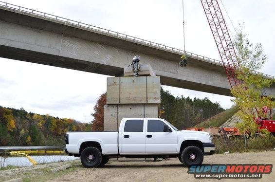 White 2006 Chevrolet Silverado 2500 parked near a bridge construction site. Crane in background