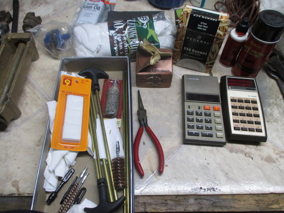 Gun cleaning kit with rods, brushes, and patches, alongside two calculators and ammunition boxes