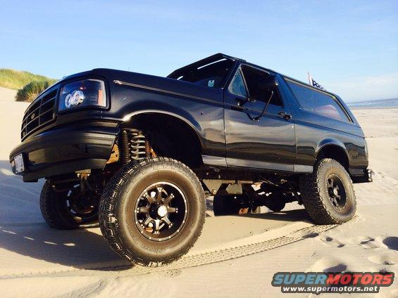 Black 1992 Ford Bronco with lifted suspension and aftermarket wheels on a sandy beach