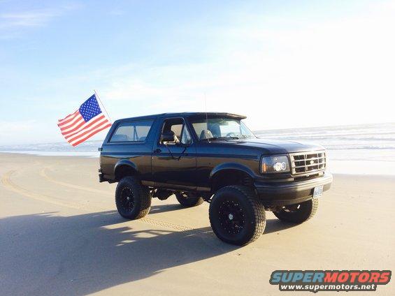 Black 1992 Ford Bronco with American flag on beach