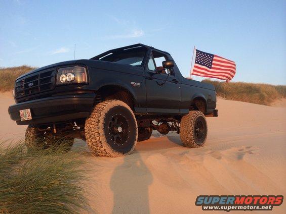 1992 Ford Bronco with American flag on sand dunes, lifted with off-road tires