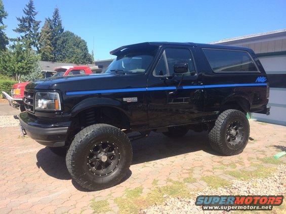 Black lifted 90s Ford Bronco with blue stripe and black wheels in driveway