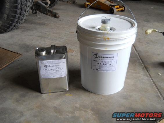 Two containers of US Composites urethane pour foam, one metal can and one white bucket, on a concrete floor