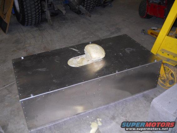 Metal box with a hole and a beige object on top, in a garage with tires and equipment in the background