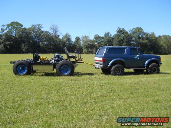 Blue Ford Bronco towing a custom chassis with a seat and engine on it