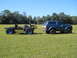 1992 Ford Bronco - A blue Ford Bronco tows a custom-built chassis with a seat and engine across a grassy field.