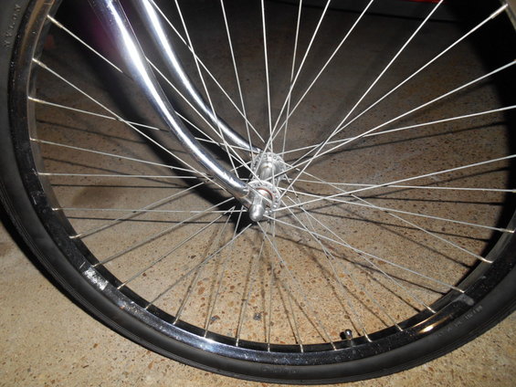 Chrome bicycle wheel with thin spokes and black tire on concrete