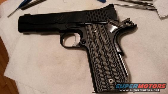 black pistol with textured grips on a white cloth, tools in background