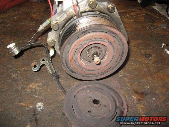 Car AC compressor clutch assembly disassembled on a wooden surface. The pulley and clutch plate are separate